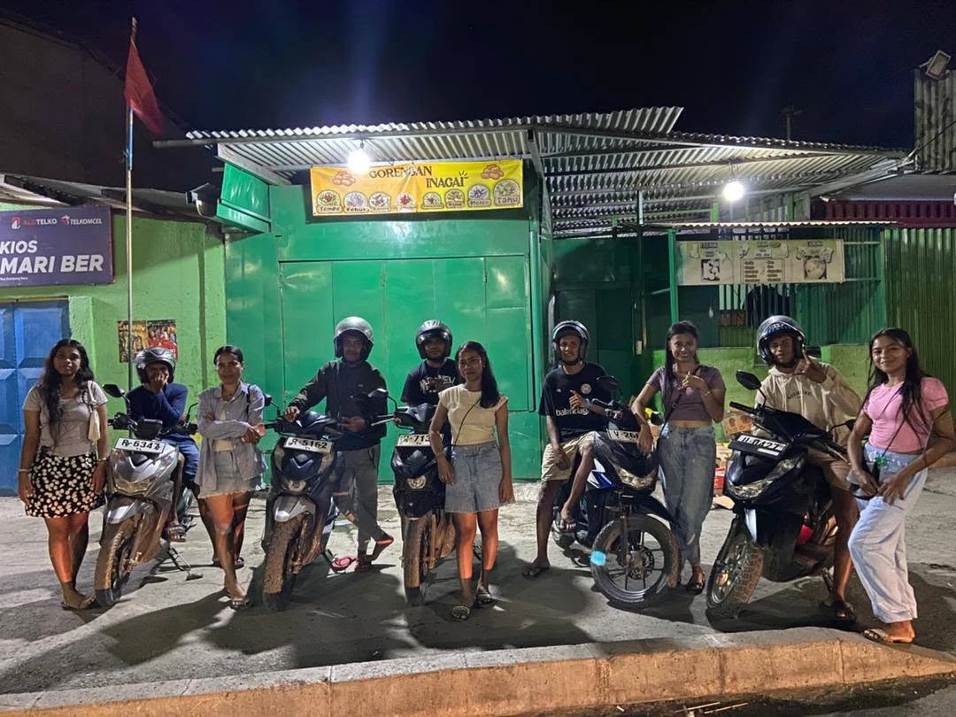 A group of TULA-HAU drivers and riders with motorbikes outside a shop at night