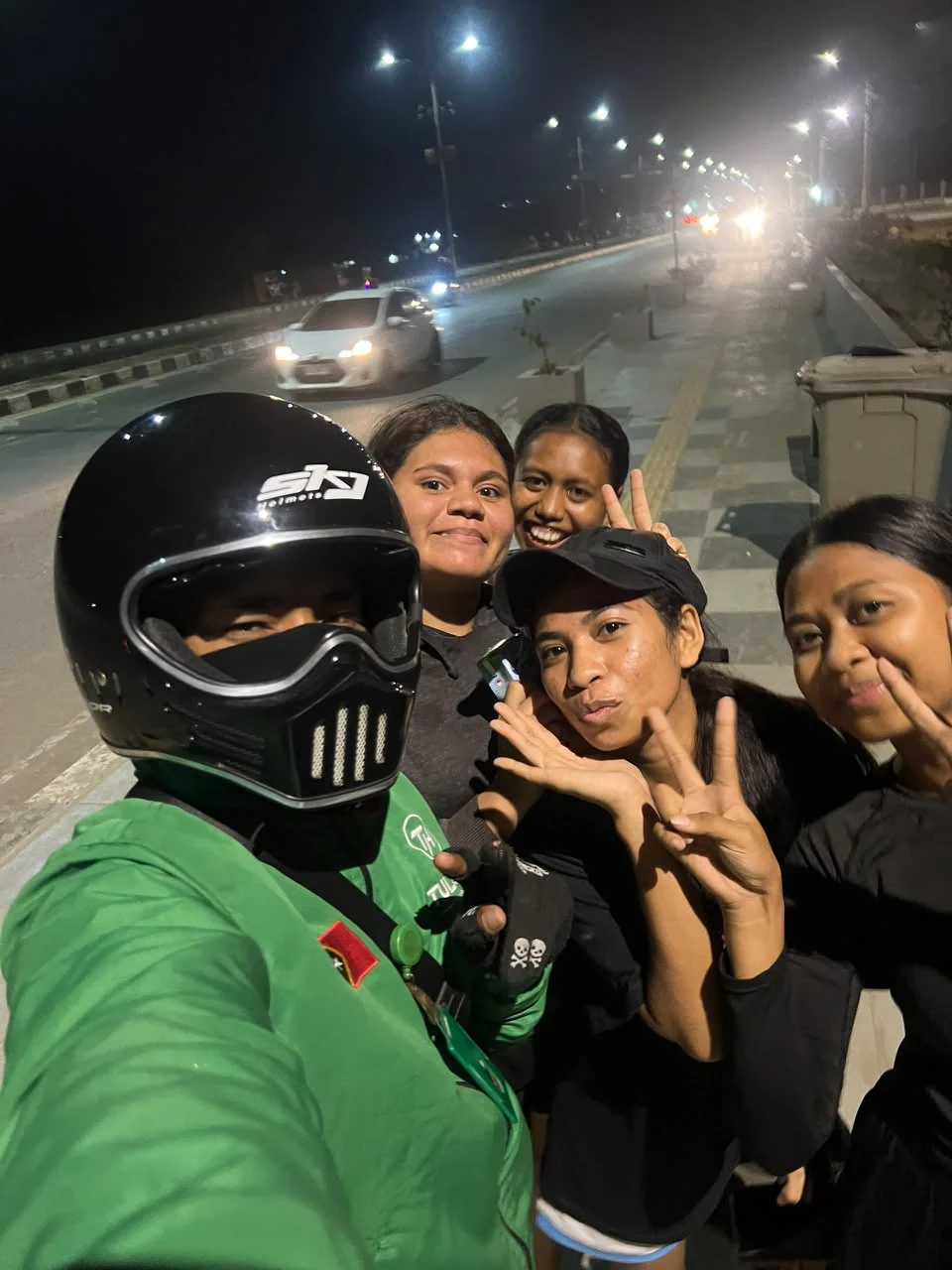 A TULA-HAU driver in a helmet taking a night-time selfie with smiling passengers