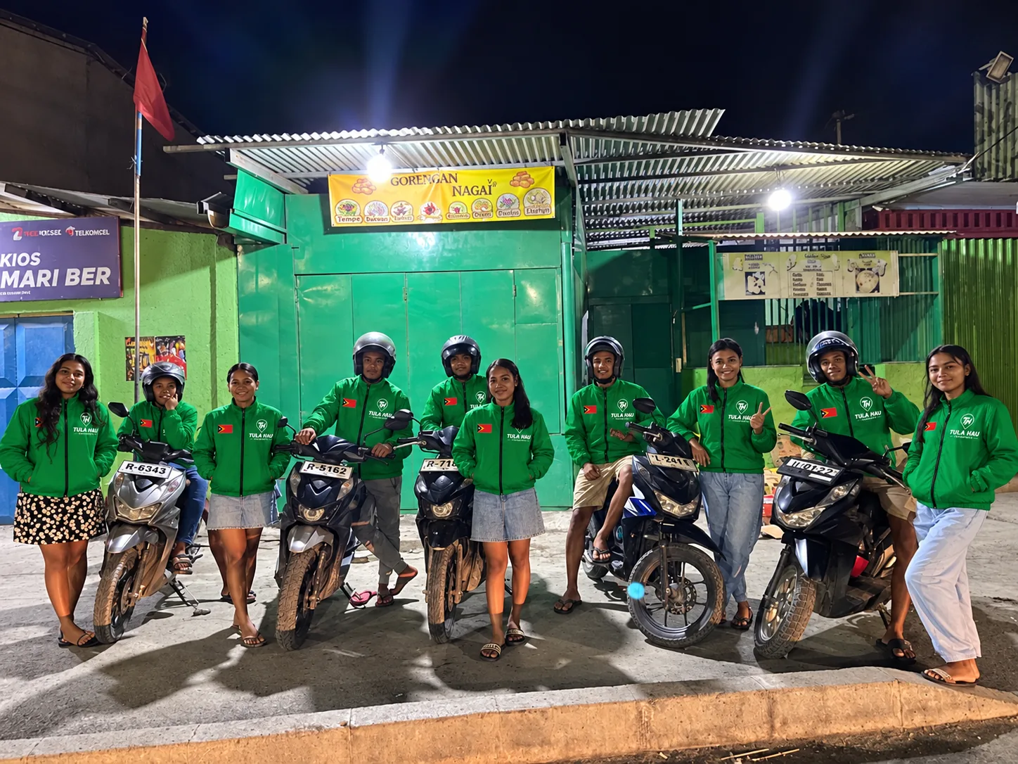 TULA-HAU drivers in green jackets with their motorbikes outside a shop at night